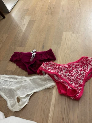 3-pack spetsiga trosor i olika färger NYTT - Säljer ett 3-pack trosor i olika färger och material. Helt nya aldrig använda. Ett par är vinröda i spets med blommönster, ett par är vita och transparenta med små prickar och spetskant, och ett par är rosa med blommigt spetsmönster. Alla har en feminin och ungdomlig design.
