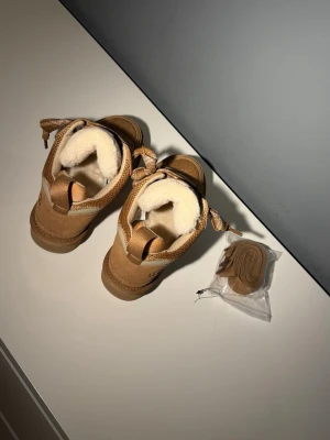 Beige sneakers från UGG med foder - Snygga beige sneakers från UGG med grov sula och fluffigt vitt foder på insidan. Ovandelen är i mocka och textil, och skorna har matchande beige skosnören samt extra snören medföljer. Perfekta för dig som vill ha både stil och komfort.