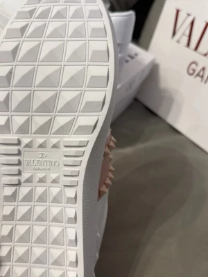 Vita Valentino Garavani sneakers - Snygga vita sneakers från Valentino Garavani med coola nitar på sidan och klassisk logga på sulan och innersulan. Skorna har en chunky sula i gummi och är tillverkade i slätt läder. Perfekta för dig som vill ha en exklusiv och trendig look.