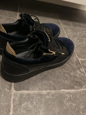 Giuseppe Zanotti  - Box följer med!Säljer ett par lyxiga sneakers från Giuseppe Zanotti i mörkblå sammet och svart skinn. Har ej kvitto. Skorna har guldfärgade dragkedjor och logga på plösen, samt snörning och platt sula. Grym design som sticker ut och passar dig som gillar exklusiva detaljer.