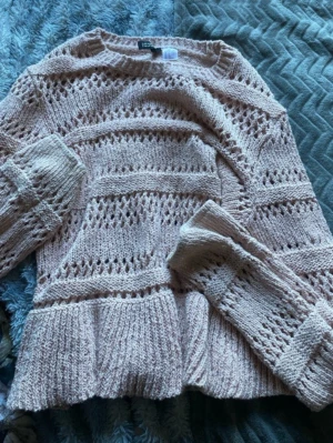 Ljusrosa stickad tröja med volang - Supersöt ljusrosa stickad tröja från HM med genombrutet mönster och volangkant nedtill. Tröjan har långa ärmar och en avslappnad passform, perfekt för att höja mysfaktorn. Materialet känns mjukt och stretchigt.