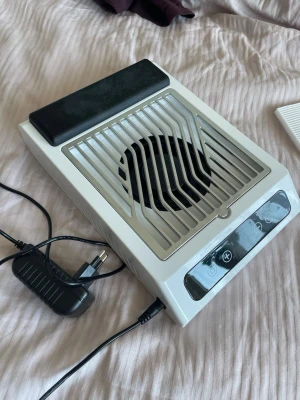 Elektrisk dammsugare för naglar - Elektrisk dammsugare för naglar i vit plast med svart handledsstöd och metallgaller. Har touchknappar för styrning och medföljer filter samt strömadapter. Perfekt för att hålla nagelstationen fri från damm under manikyr och nagelförlängning.