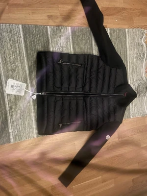 Svart pufferjacka från Moncler - Snygg svart pufferjacka från Moncler med quiltad kropp och släta ärmar. Jackan har dragkedja framtill, två dragkedjeförsedda fickor och en Moncler-logga på ärmen. Perfekt för kyligare dagar och ger en stilren look.