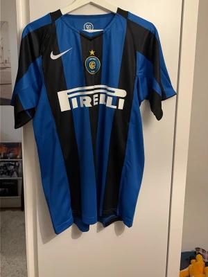 Inter Milan matchtröja Nike blå/svart - Säljer en klassisk Inter Milan matchtröja från Nike i blått och svart med vertikala ränder. Tröjan har klubbmärke, Nike-logga och Pirelli som sponsor framtill. Tillverkad i lätt och ventilerande material, perfekt för fotboll eller träning.