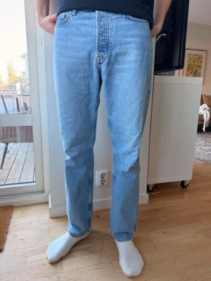 Ljusblå raka jeans från samsoe samsoe - Säljer ett par klassiska ljusblå jeans från samsoe samsoe med rak passform och hög midja. Jeansen har fem fickor, gylf med dragkedja och knapp samt ett ikoniskt läderpatch bak i midjan. Perfekta för en avslappnad och trendig look. Modellen är 186 cm och väger 75 kg