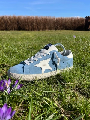 Blåa sneakers från Golden Goose - Snygga blåa sneakers från Golden Goose med vit stjärndetalj på sidan, vita skosnören och vit sula. Ovandelen är i mocka och hälen har en vit kontrast. Perfekta sommar- och vårsneakers. Tveka inte på att höra av dig ifall du undrar något!✨