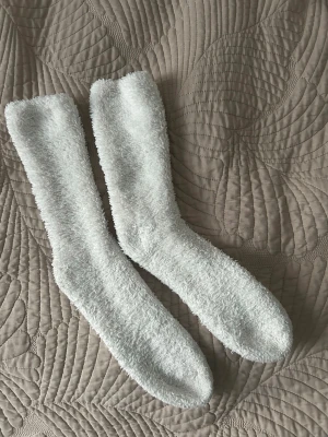 Vita fluffiga myssockor - Supermjuka och fluffiga vita sockor som är perfekta för att hålla fötterna varma hemma. Långa och gosiga, tillverkade i ett mjukt syntetmaterial som känns riktigt skönt mot huden. Perfekta för kalla dagar när du vill mysa till det.