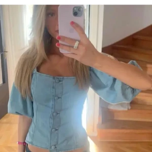 Ljusblå jeanskorsett med knappar😚😚 - Snygg ljusblå korsett i jeansmaterial med knappar framtill. Toppen har korta puffärmar och en fyrkantig urringning. Perfekt för en trendig look.