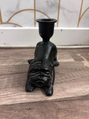 Svart bulldogg ljusstake i metall - Unik ljusstake i form av en bulldogg, gjord i svartmålad metall. Ljushållaren sitter på hundens rygg och hela figuren har tydliga detaljer som markerar ansiktet och tassarna. Perfekt för dig som gillar annorlunda inredningsdetaljer.finns lite stearinljus stänk på den