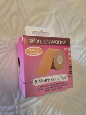 Brushworks Body Tape Caramel 5m - 5 meter kroppstejp från Brushworks i nyansen 3.0 Caramel. Perfekt för att forma och hålla kläder på plats. Kommer i en praktisk rosa förpackning och är PETA-godkänd. Passar för olika hudtoner enligt nyanskartan på sidan av förpackningen.