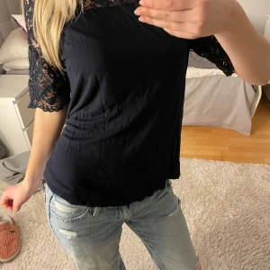 Marinblå topp med spetsärmar - Snygg marinblå topp från Lindex med korta spetsärmar och spetsdetaljer över axlar och bröst. Toppens kropp är i mjukt tyg och har en feminin passform. Perfekt att styla med jeans eller kjol för en trendig look. Storleken är i M men skulle säga att den passar S. 