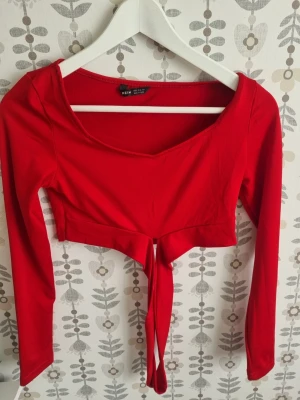 Röd croppad topp med knyt - Trendig röd croppad topp från New Yorker med långa ärmar och snygg knytning framtill. Toppen har en djupare rundad ringning och är perfekt för dig som vill ha en statement piece i garderoben.