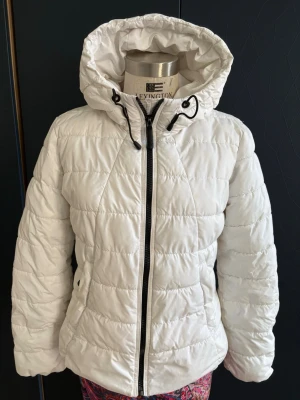 Vit dunjacka med huva Lexington - Snygg vit dunjacka från PB Sister med quiltad design och dragkedja framtill. Materialet är ger en fräsch look.