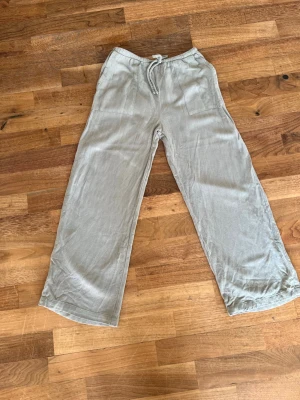 Ljusgröna vida linnebyxor - Säljer ett par ljusgröna linnebyxor med bred passform och dragsko i midjan. Byxorna har två stora fickor framtill och är tillverkade i ett svalt linnematerial. Perfekta för en avslappnad och trendig look.