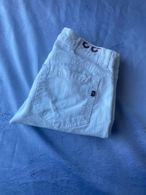 Dondup George -W33 - Säljer ett par vita jeans från dondup med klassisk rak passform. Jeansen har fem fickor, synliga sömmar och den ikoniska Evisu-loggan broderad på bakfickan. Tillverkade i kraftig denim som ger en snygg och stilren look. Korta i längden cirka 29/30 Längd och Waist 33.