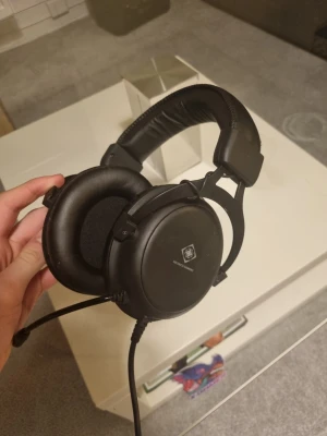 Svarta over-ear hörlurar QPAD - Säljer ett par svarta over-ear hörlurar från QPAD med inbyggd mikrofon. De har mjuka, vadderade öronkuddar i konstläder och justerbart huvudband för extra komfort. Perfekta för gaming eller långa samtal online.