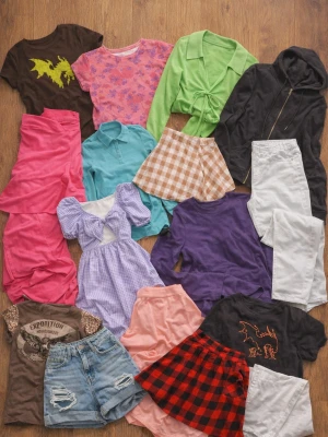 Mixat Fairycore & Streetwear-paket – 14 plagg i olika stilar - Säljer ett klädpaket med 14 snygga plagg i varierade färger och stilar – perfekt för dig som gillar att mixa fairycore, Y2K och streetwear!    Innehåller bland annat:   - Flera grafiska T-shirts (drake, örn, textmotiv)   - Färgglada toppar och blusar i grönt, rosa, blått och lila   - Kjolar i olika modeller (plisserad, rutigt, midi)   - Jeans och shorts med hög midja   - En svart hoodie för en mer avslappnad look    Alla plagg är i fint skick, vissa lätt använda men utan större defekter. 