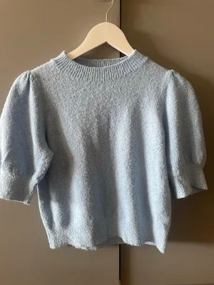 Ljusblå stickad topp Vero Moda - Supersöt ljusblå stickad topp från Vero Moda med puffärmar och ribbad rund hals. Kortare modell med halvlånga ärmar, perfekt till jeans eller kjol. Mjuk och skön kvalitet som känns lyxig och trendig.