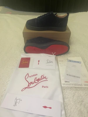 Blåa sneakers från Christian Louboutin - Säljer ett par mörkblå sneakers från Christian Louboutin med klassisk röd sula och snygg snörning. Ovandelen är i mocka och insidan i beige skinn. Skorna kommer med originalkartong, dustbag och äkthetskort. Perfekta för dig som vill ha något exklusivt och stilrent.