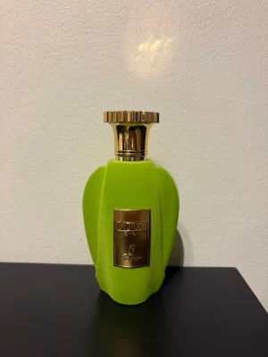 Grön parfymflaska från Moresque - Unik parfymflaska från Moresque i en klar grön färg med sammetslen yta och guldfärgad kork. Flaskan har en elegant, rundad form och en guldfärgad metallplatta med märkets logga på framsidan. Perfekt för dig som gillar exklusiva dofter.