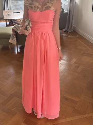 Axelbandslös långklänning i rosa - Säljer en elegant axelbandslös långklänning i en härlig coral nyans. Det här är en balklänning jag bar förra året, super fin! Skriv privat för fler bilder!