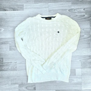 Morris Stockholm Cable Knit Sweater 🔥 - Fin vit cable knit tröja från Morris Stockholm med klassisk flätstickning över hela och litet broderat lilja-logo på bröstet. Tjock, skön kvalitet som känns lyxig och tidlös – perfekt för vardag eller lite finare look. Storlek: M  Mått (platt): Axelbredd: ca 48–50 cm Pit to pit: ca 51–53 cm Längd: ca 66–68 cm Skick: Mycket bra skick – knappt använd och fortfarande snygg. En liten tråd har gått upp pyttelite längre ner på magen (typ en liten ögla, inget som syns vid användning. Packas säkert