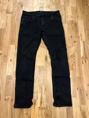 Svarta slim fit jeans från Smog - Säljer ett par svarta slim fit jeans från Smog med klassisk femficksmodell och knappgylf. Jeansen har raka ben och diskreta sömmar, perfekta till en avslappnad streetstil. Materialet är mjukt och stretchigt för extra komfort.