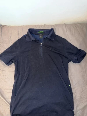 Hugo boss piké  - Snygg mörkblå polotopp från BOSS med halv dragkedja framtill och klassisk krage. Toppen har korta ärmar och är tillverkad i mjuk bomull. Perfekt för en stilren och avslappnad look.