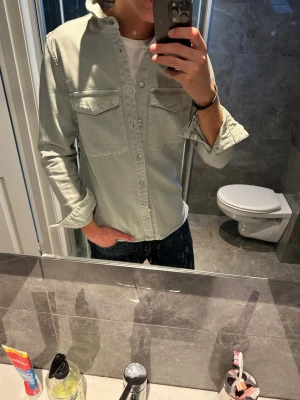 Ljusgrön overshirt med fickor - Snygg ljusgrön overshirt med två bröstfickor och knäppning framtill.  Den är i riktigt bra skick inga tecken på användning. Jag på bilden är 188cm och bär storlek S. Hör av er vid vidare frågor:)