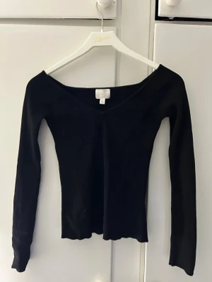 Svart ribbad långärmad topp - Svart långärmad topp med v-ringning och ribbad struktur. Sitter tight och har en enkel, stilren design som passar till det mesta. Perfekt att styla med jeans eller kjol för en snygg look.