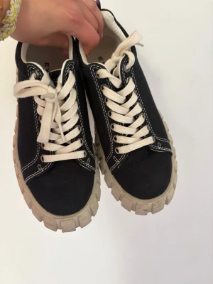 Svarta Eytys sneakers - Svarta sneakers från Eytys med vit kontrastsöm och ”traktorsula”. Skorna har vita snören och en lila hälflik. Nästintill oanvända! 