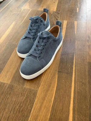 Christian Louboutin Skor - Stilrena blå sneakers med vit sula och röd undersida. Skorna har klassisk låg profil, rund tå och är tillverkade i mockaliknande material. Perfekta för dig som vill ha en clean look med en cool detalj under foten. Matcha med jeans eller shorts för en avslappnad vibe.