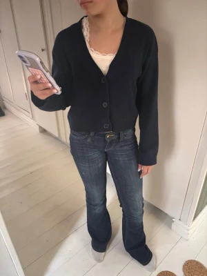 Mörkblå kofta från H&M - Mörkblå kofta från H&M med v-ringning och tre knappar framtill. Modellen är lite kortare och har långa ärmar. Perfekt att slänga över ett linne eller t-shirt. Enkel och stilren design som passar till mycket. Samt aldrig använd, har tyvärr inte kvar prislappen