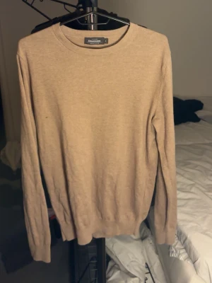 Beige stickad tröja - En stilren beige tröja från Dimissione Danza med rund halsringning och långa ärmar. Tröjan har en enkel och klassisk design med ribbade muddar vid ärmslut och nederkant. Perfekt för en avslappnad och snygg look.
