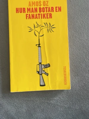 Hur man botar en fanatiker bok - Gul bok med titeln 'Hur man botar en fanatiker' av Amos Oz. Omslaget har en illustration av ett gevär som övergår i en olivkvist. Boken är på svenska och utgiven av Teskedsorden. Perfekt för dig som gillar samhällsfrågor och vill läsa om fanatism.