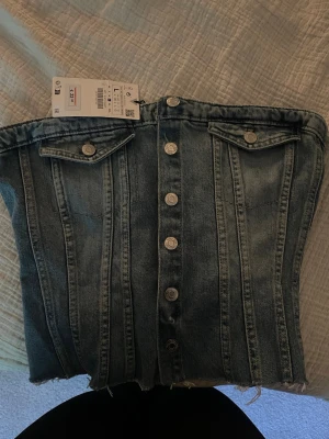 Denim tubtopp med knappar från ZARA - Cool tubtopp i blå denim från ZARA med knappar framtill och två dekorativa bröstfickor. Toppen har även smock ibak💕 stl L men skulle säga mer om en M, oanvänd🥰