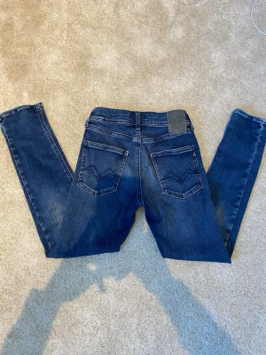Replay hyperflex slim jeans mörkblå - Snygga mörkblå slim jeans från Replay med klassisk femficksdesign och diskreta slitningar. Replay slim hyperflex  Jeansen har smal passform och normal midja, samt detaljerade bakfickor med broderi. Perfekta för en trendig och avslappnad stil. 