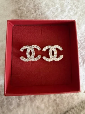 örhängen - örhängen i guldtonad metall med gnistrande strass-stenar. Örhängena har den klassiska dubbla C-loggan