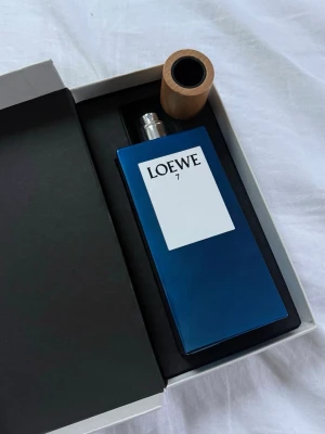 Loewe 7  - Loewe 7 Eau de Toilette i en stilren, mörkblå rektangulär flaska med trälock och vit etikett. Parfymen kommer i originalförpackning och rymmer 100 ml. En modern och elegant doft från Loewe, perfekt för dig som gillar exklusiva parfymer.