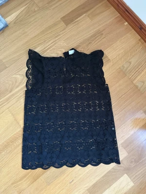 Svart spetsblus med volangärm - Supersnygg svart blus i spets med volangärmar och rund hals. Blusen är ärmlös och har ett feminint, transparent mönster med fina detaljer. Man kan även ha linne under om man inte vill ha den så genomskinlig! Storlek är M men passar även S 