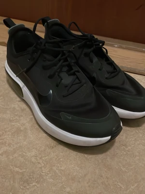 Svarta Nike sneakers med vit sula - Snygga svarta Nike sneakers med vit, tjock sula och diskret Swoosh-logga på sidan. Ovandelen är i syntetmaterial och mesh för en modern look. Skorna har svarta skosnören och låg profil som passar till streetwear.