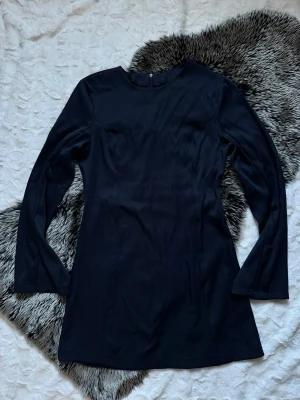 Mörkblå långärmad kortklänning - En stilren mörkblå klänning med lång ärm och rund halsringning. Klänningen är kort i modellen och har en enkel, elegant design utan synliga detaljer eller mönster. Perfekt för dig som gillar minimalistisk stil.