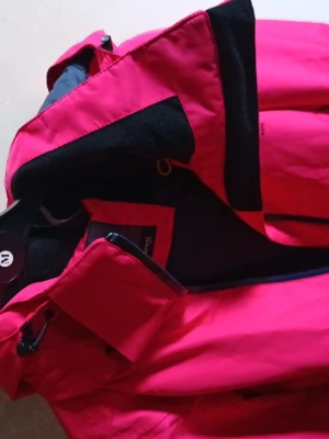 Rosa vindjacka från Everest - Snygg rosa vindjacka från Everest med svarta detaljer och meshfoder på insidan. Jackan har dragkedja framtill, hög krage och justerbar huva. Perfekt för blåsiga dagar och outdoor-aktiviteter.