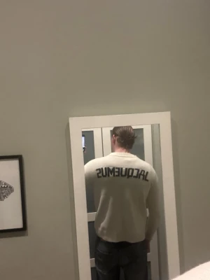Vit stickad tröja från Jacquemus - Säljer en stilren vit stickad tröja från Jacquemus med svart logotyp på ryggen. Tröjan har rund halsringning och ribbstickade muddar vid ärmslut och nederkant. Perfekt för dig som gillar minimalistisk design och vill ha något trendigt i garderoben.
