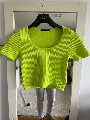 Neongul ribbad topp från Dunnes  - Superfräsch neongul ribbad topp från Dunners  med korta ärmar och rund halsringning. Modellen är croppad och har en stretchig passform som sitter snyggt på kroppen. Perfekt för dig som vill sticka ut med färg!
