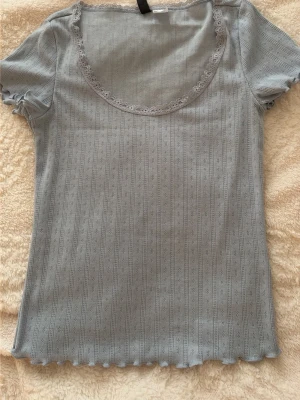 Ljusblå ribbad topp med spetskant - Supersöt ljusblå topp med ribbad struktur och diskret mönster. Rund halsringning med spetskant och korta ärmar med volangdetalj. Perfekt att styla med jeans eller kjol för en chill look.