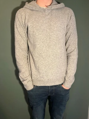 Ljusgrå hoodie i mjukt material - En stilren ljusgrå hoodie med huva och lång ärm. Hoodien är tillverkad i ett mjukt och bekvämt tyg, perfekt för en avslappnad look. Inga synliga loggor eller tryck, vilket gör den enkel att matcha med olika outfits. Nypris ca 1000 kr