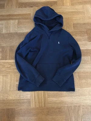 Mörkblå hoodie från Polo Ralph Lauren - Snygg mörkblå hoodie från Polo Ralph i storlek L barnstorlek passar ca155-170. Liten vit logga broderad på bröstet. Perfekt för en avslappnad och stilren look. Tillverkad i mjukt material för extra komfort. Obs priset är ej hugget i sten