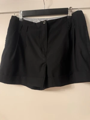 Svarta klassiska shorts med fickor - Snygga svarta shorts med normal passform och diskreta fickor både fram och bak. Stängs med knapp och dragkedja framtill. Perfekta till sommaren och lätta att matcha med olika stilar.