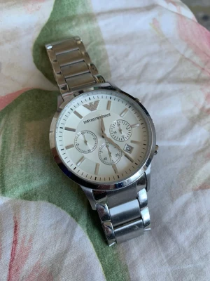 Emporio Armani silverfärgad klocka - Stilren klocka från Emporio Armani i silverfärgat metallarmband och vit urtavla. Ingen box bara klockan. Nypris över 1500 säljer för endast 400